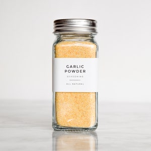 May include: A glass jar with a silver lid filled with yellow garlic powder. The label reads "Garlic Powder Seasoning All Natural".