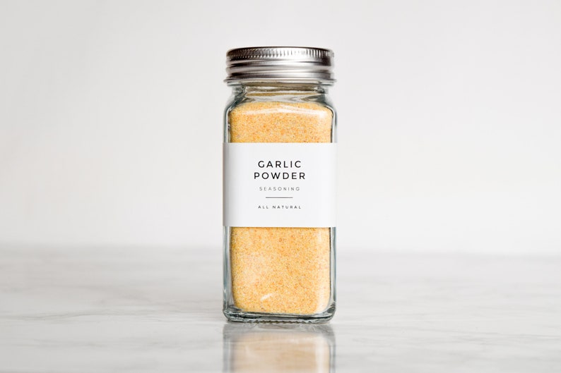 May include: A glass jar with a silver lid filled with yellow garlic powder. The label reads "Garlic Powder Seasoning All Natural".