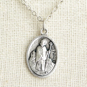 May include: Silver oval pendant necklace featuring a depiction of Saint Patrick holding a staff. The pendant has the text "St. Patrick" inscribed on the right side.