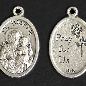 May include: Silver oval pendant with a depiction of Saint Joseph holding the baby Jesus. The back of the pendant reads "Pray for Us Italy".
