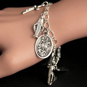 Op de afbeelding: Een zilveren armband met meerdere bedels, waaronder een kruis, een figuur van de Maagd Maria en een afbeelding van Sint-Joris die de draak verslaat.