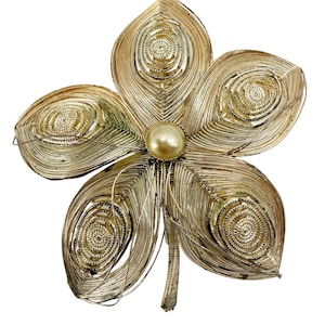 May include: A gold-tone metal brooch shaped like a five-petaled flower. Each petal features intricate wire filigree work with a central spiral pattern. A single, round, cream-colored faux pearl is set at the center of the flower, and a thin stem extends from the base.