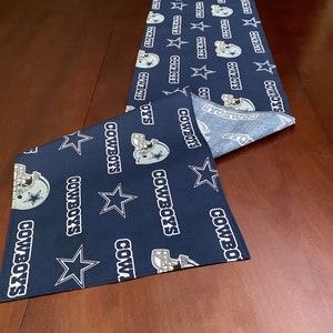 K&ouml;nnte beinhalten: Ein dunkelblauer Tischl&auml;ufer mit einem sich wiederholenden Muster aus wei&szlig;en Sternen, dem Logo der Dallas Cowboys und dem Wort "COWBOYS".