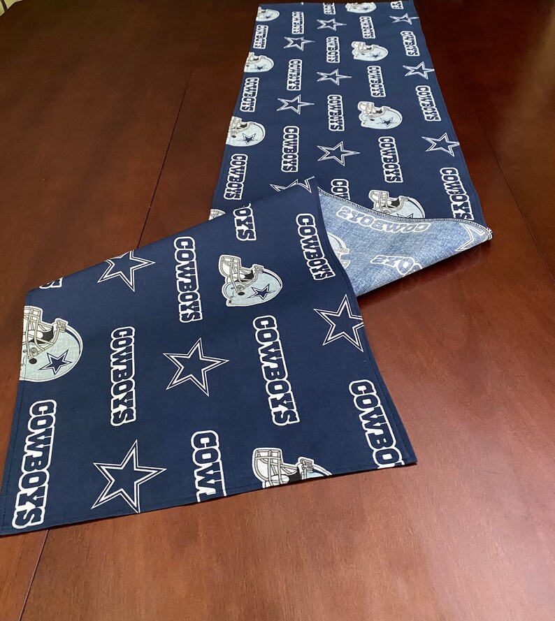 K&ouml;nnte beinhalten: Ein dunkelblauer Tischl&auml;ufer mit einem sich wiederholenden Muster aus wei&szlig;en Sternen, dem Logo der Dallas Cowboys und dem Wort "COWBOYS".