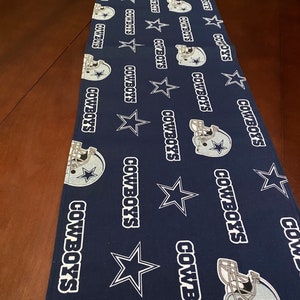 K&ouml;nnte beinhalten: Ein blauer Tischl&auml;ufer mit einem sich wiederholenden Muster aus wei&szlig;en Sternen, den Worten "COWBOYS" und einem Footballhelm.