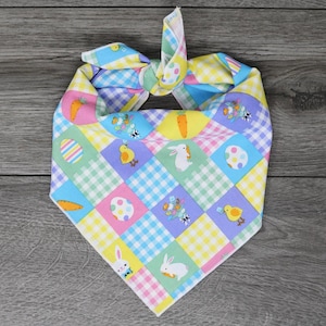 May include: A colorful Easter-themed bandana with a checkered pattern and images of bunnies, chicks, and eggs. The bandana is tied in a knot at the top.