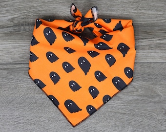 May include: Orange bandana with a black ghost pattern. The bandana is tied in a knot at the top.