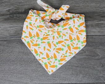 May include: A white bandana with a pattern of orange carrots and white flowers. The bandana is tied in a knot at the top.