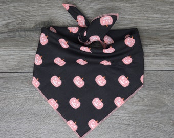 May include: A black bandana with a pink pumpkin pattern. The bandana is tied in a knot at the top.