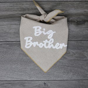 May include: A beige bandana with a gold trim and the words "Big Brother" embroidered in white.