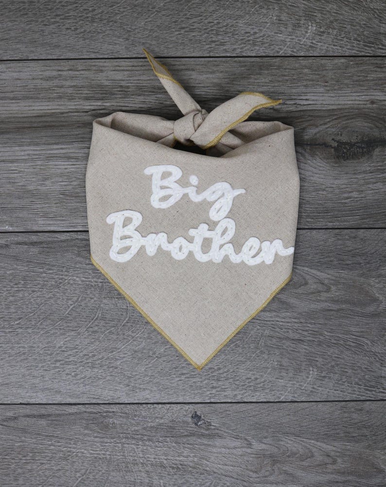 May include: A beige bandana with a gold trim and the words "Big Brother" embroidered in white.