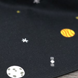 Puede incluir: Tela negra con estrellas, planetas y un sat&eacute;lite bordados en blanco. La tela tiene una textura sutil.