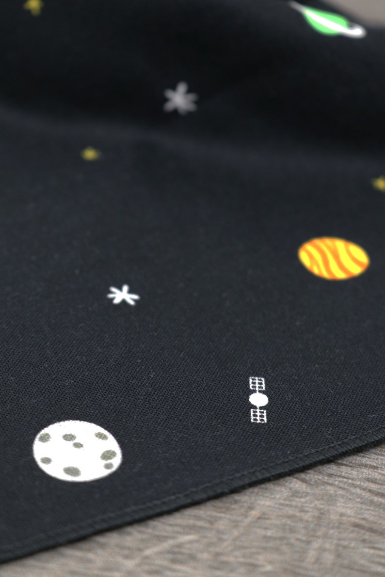 Puede incluir: Tela negra con estrellas, planetas y un sat&eacute;lite bordados en blanco. La tela tiene una textura sutil.