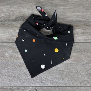 Puede incluir: Bandana negra con tem&aacute;tica espacial con planetas, estrellas y un sat&eacute;lite. La bandana est&aacute; anudada.