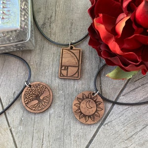 May include: Three wooden necklaces with different pendants. The first pendant is a rectangle with the Fibonacci sequence and the Golden Ratio. The second pendant is a circle with a tree of life design. The third pendant is a circle with a sun and moon design.