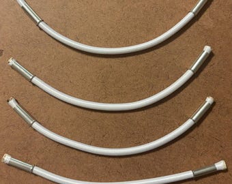 May include: Four white, flexible tubes with metal ends are arranged in a curved pattern on a brown surface. The tubes have a ribbed texture and are slightly curved. The metal ends are silver in color.