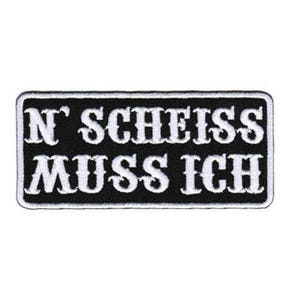 May include: A rectangular black and white embroidered patch. The patch features the German phrase "N' Scheiss Muss Ich" in white, stylized lettering. The patch has a black border and is set against a white background.