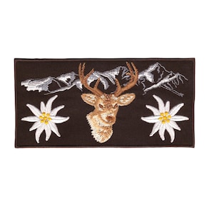 Op de afbeelding: Geborduurde patch met een bruin hertenhoofd, witte edelweiss bloemen en een bergketen op de achtergrond. De patch is op een bruine stof.