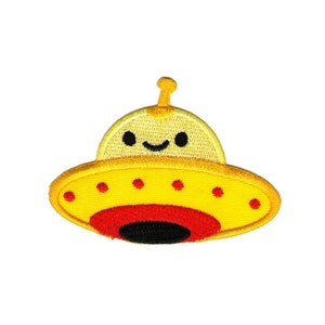 Könnte beinhalten: Ein gelber gestickter Bügelaufkleber mit einem lächelnden Cartoon-UFO mit roten und schwarzen Details.
