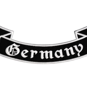 Könnte beinhalten: Ein schwarz-weißer, gestickter Aufnäher in Form eines Banners. Das Wort "Germany" ist in weißen, gotischen Buchstaben gestickt. Das Banner hat eine gebogene Form mit spitzen Enden.