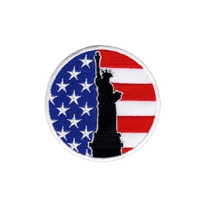 Peut inclure: Un écusson rond brodé avec un contour blanc. L'écusson représente une silhouette de la Statue de la Liberté devant un drapeau américain. Le drapeau est rouge, blanc et bleu avec des étoiles sur la partie bleue et des rayures sur la partie rouge et blanche.