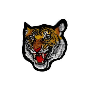 Könnte beinhalten: Gestickter Bügel-Patch mit dem Gesicht eines Tigers mit offenem Maul, das scharfe Zähne zeigt. Der Tiger hat orange und schwarze Streifen und eine weiße Schnauze.