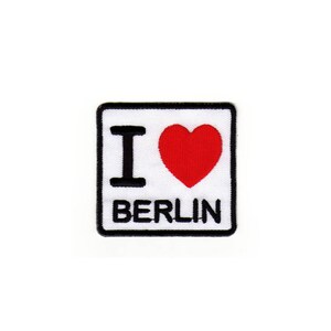 Könnte beinhalten: Weißer quadratischer Patch mit schwarzem Rand und dem Text "Ich liebe Berlin" mit einem roten Herzen in der Mitte.