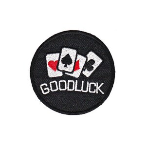Op de afbeelding: Zwarte en witte geborduurde patch met drie speelkaarten en de tekst "GOODLUCK" in wit.