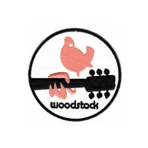 Peut inclure: Un patch circulaire blanc avec un contour noir. À l'intérieur du cercle se trouve un oiseau rose tenant une guitare noire avec le mot "Woodstock" écrit en dessous.