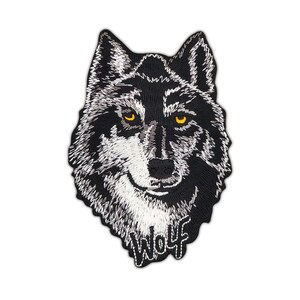 Könnte beinhalten: Schwarzer und weißer gestickter Aufnäher mit dem Gesicht eines Wolfes mit gelben Augen. Das Wort "Wolf" ist unterhalb des Wolfskopfes gestickt.