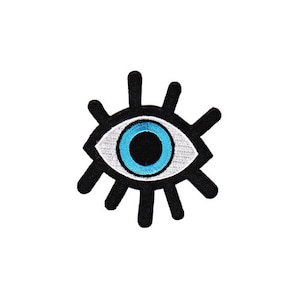 Op de afbeelding: Een geborduurd oog in zwart en wit met een blauwe iris en een witte pupil. Het oog heeft wimpers en is een populair symbool voor bescherming.