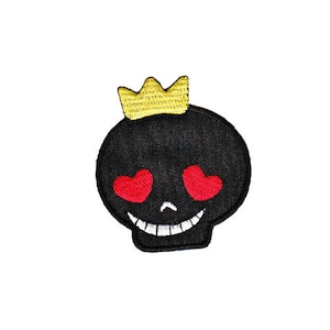 Puede incluir: Cráneo negro con una corona dorada y corazones rojos por ojos. El cráneo sonríe.