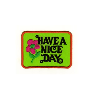 Puede incluir: Parche bordado verde con borde rojo. El parche presenta una flor rosa con un tallo verde y el texto "HAVE A NICE DAY".
