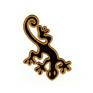 Könnte beinhalten: Schwarzer und goldener gestickter Aufnäher mit einem stilisierten Eidechsen mit einem eingerollten Schwanz.