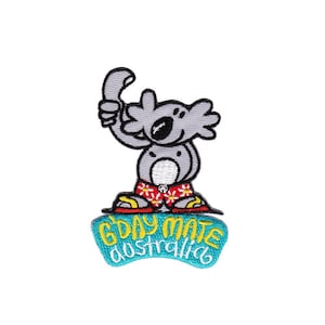 Könnte beinhalten: Gestickter Aufnäher mit einem Cartoon-Koala, der rote Shorts mit weißen Blumen trägt und eine Hand in einer 'G'day mate'-Geste hochhält. Der Koala steht auf einem blauen und gelben Banner mit dem Text 'G'day mate Australia'.