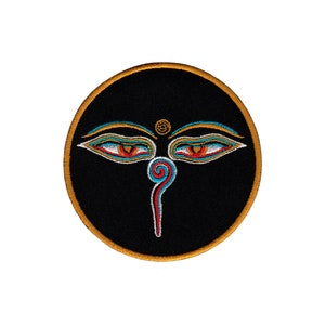 Op de afbeelding: Ronde geborduurde patch met het Boeddha-oog-ontwerp. De patch heeft een zwarte achtergrond en een gouden rand. Het oogontwerp is in rood, blauw en goud. Geschikt voor toepassing op kleding of accessoires, dit is een decoratief item.