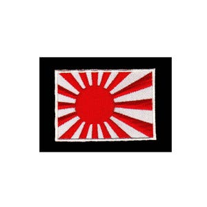 Op de afbeelding: Een geborduurde patch met de vlag van de rijzende zon van Japan. De vlag is rood en wit, met een grote rode cirkel die de zon voorstelt, omringd door 16 witte stralen.