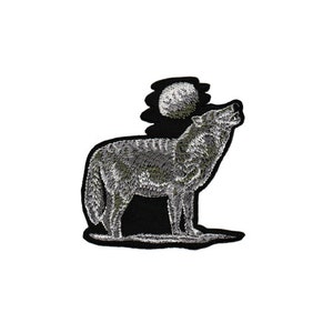 Op de afbeelding: Geborduurde strijkpatch van een wolf die huilt naar de maan. De wolf is grijs en wit, en de maan is wit tegen een zwarte achtergrond.