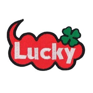 Könnte beinhalten: Roter und weißer gestickter Aufnäher mit dem Wort "Lucky" in weißer Schrift und einem grünen vierblättrigen Kleeblatt.