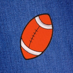 May include: Orange and white embroidered patch of an American football on a blue denim background.