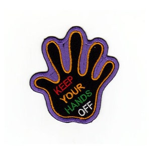 May include: Embroidered patch in the shape of a hand, with a black palm and fingers, outlined in orange and purple. The text "KEEP YOUR HANDS OFF" is embroidered in red, green, and white.