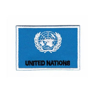 Op de afbeelding: Een blauwe geborduurde patch met het logo van de Verenigde Naties en de tekst "UNITED NATIONS" in zwart.