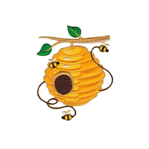 Op de afbeelding: Een geborduurde bijenkorf in geel en bruin met een kleine ingang en drie bijen, hangend aan een tak met groene bladeren.