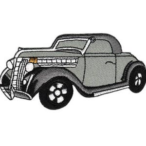 Könnte beinhalten: Ein graues Oldtimer-Auto mit schwarzem Verdeck und weißen Zierleisten. Das Auto hat einen verchromten Stoßfänger und Scheinwerfer. Das Auto ist ein klassisches Design.