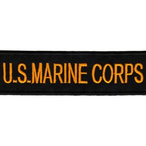 Könnte beinhalten: Ein rechteckiger, schwarzer Aufnäher mit dem goldfarbenen, gestickten Schriftzug "U.S. MARINE CORPS". Der Aufnäher ist wahrscheinlich aus strapazierfähigem Stoff gefertigt und zum Aufnähen oder Anbringen an Kleidung oder Ausrüstung bestimmt.
