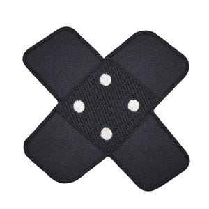 Peut inclure: Patch en tissu noir en forme de croix avec quatre points blancs au centre.