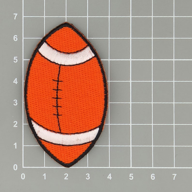May include: Orange and white felt football patch. The patch is shaped like a football and has white stitching around the edges.