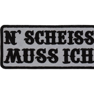 Peut inclure: Un écusson brodé gris et noir avec le texte "N' SCHEISS MUSS ICH".