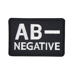 May include: A black rectangular patch with white embroidered text. The text reads "AB-" above "NEGATIVE". The patch has a black border and is likely made of fabric. The text is in a bold, sans-serif font.