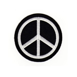 Könnte beinhalten: Ein schwarzer runder Patch mit einem aufgestickten weißen Friedenssymbol.